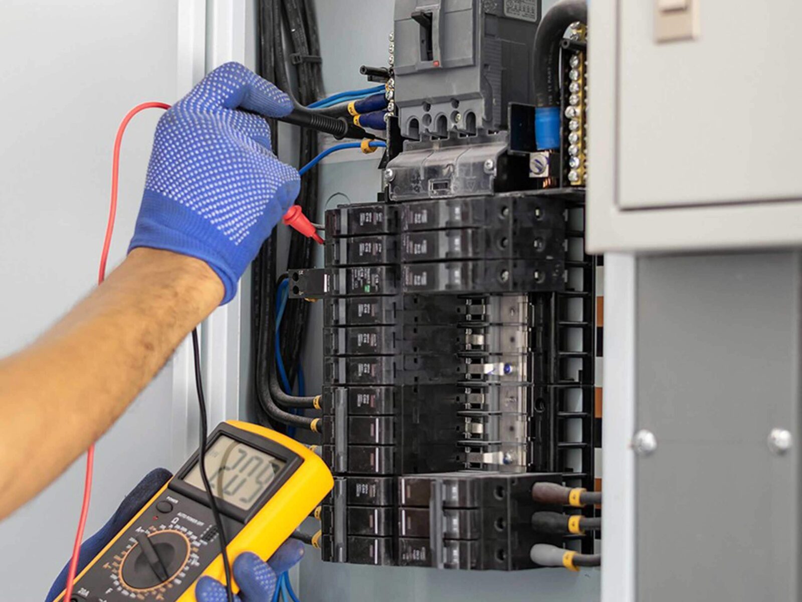A technician using a multimeter to test electrical circuits inside a circuit breaker panel.