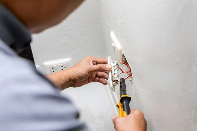 A person using pliers to work on electrical wiring connected to a wall outlet.
