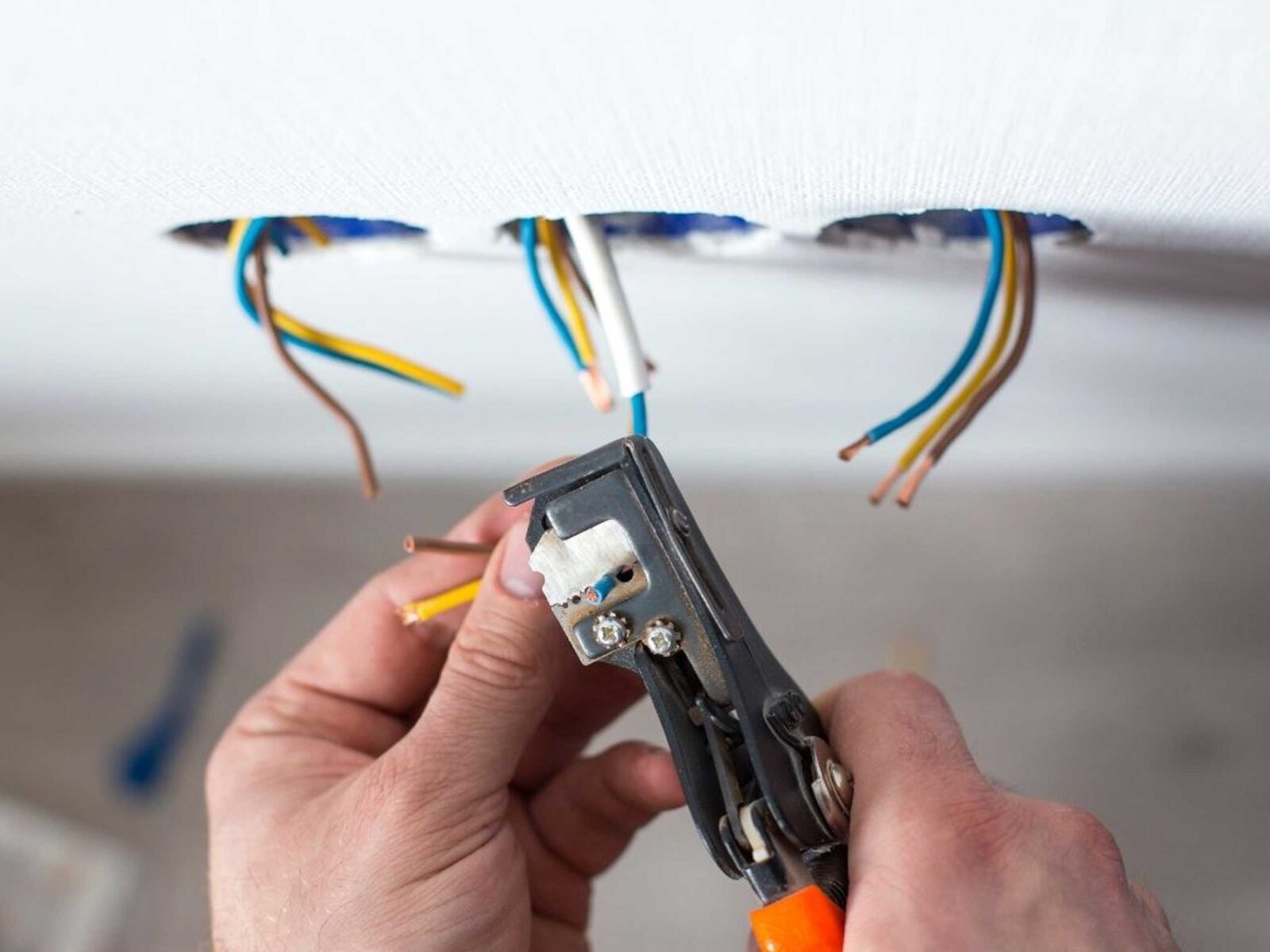 A person using wire strippers on electrical wires coming out of a wall.