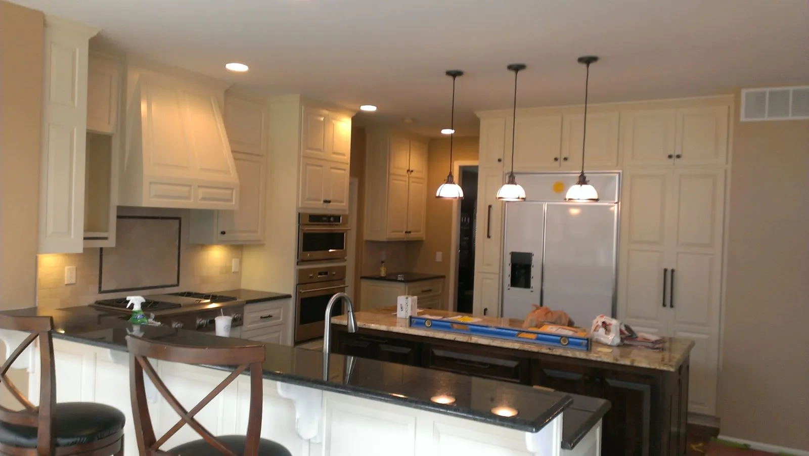 A modern kitchen with light-colored cabinets, a central island with bar stools, stainless steel appliances, and pendant lighting.