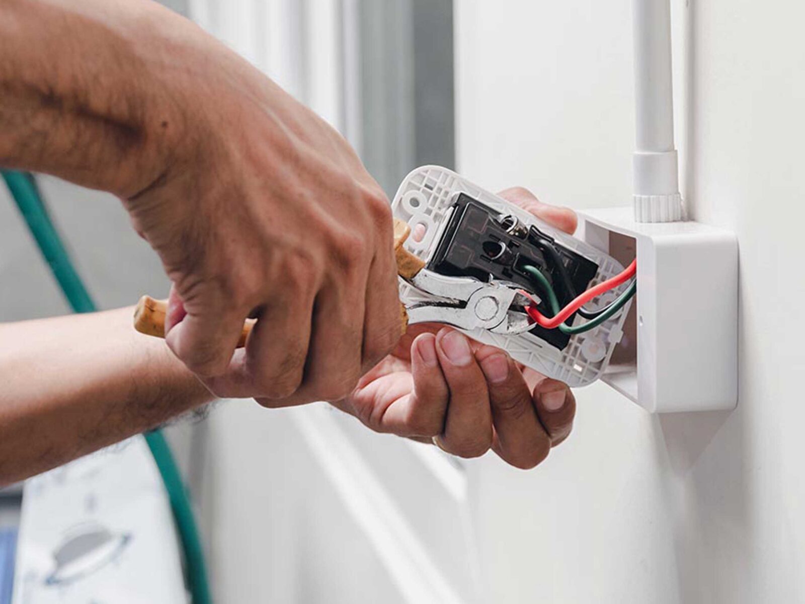 A person is working on an electrical outlet, holding a tool and exposing the wiring.