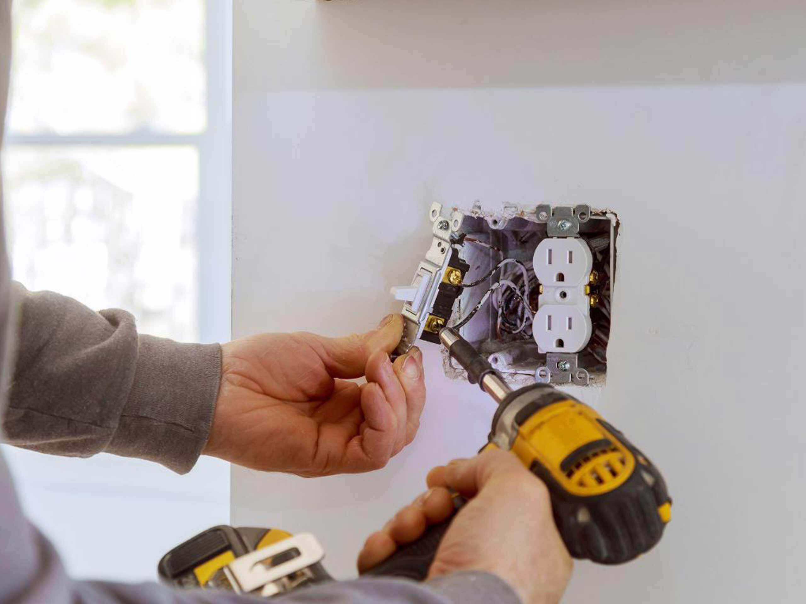 A person is working on an electrical outlet installation, using a screwdriver and a drill.