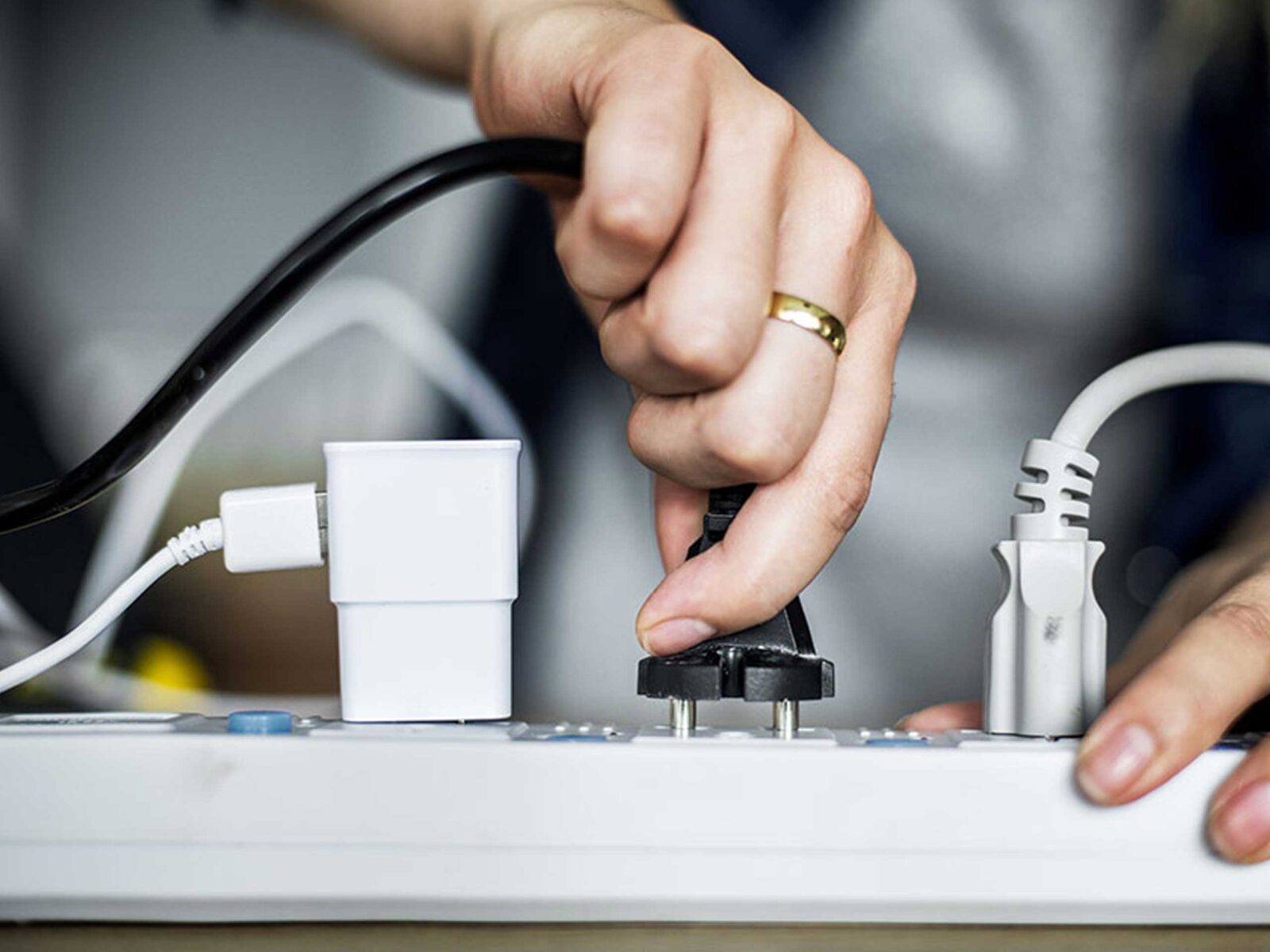 A person plugging a black electrical plug into a power strip with various cords and chargers.