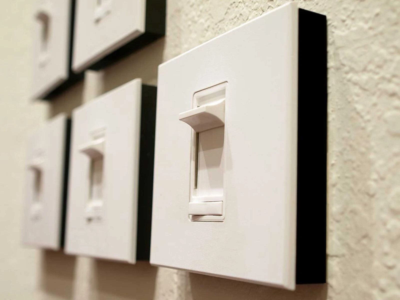 A close-up of several white light switches mounted on a textured wall.
