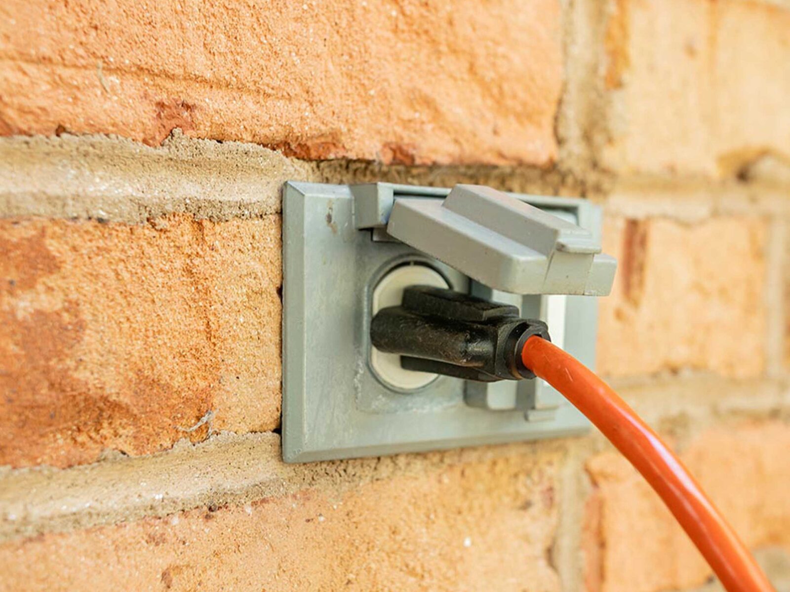 An orange electrical cord plugged into a wall outlet on a brick wall.