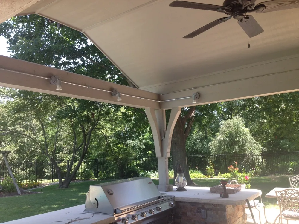 A covered outdoor patio with a grill, ceiling fan, and backyard scenery.