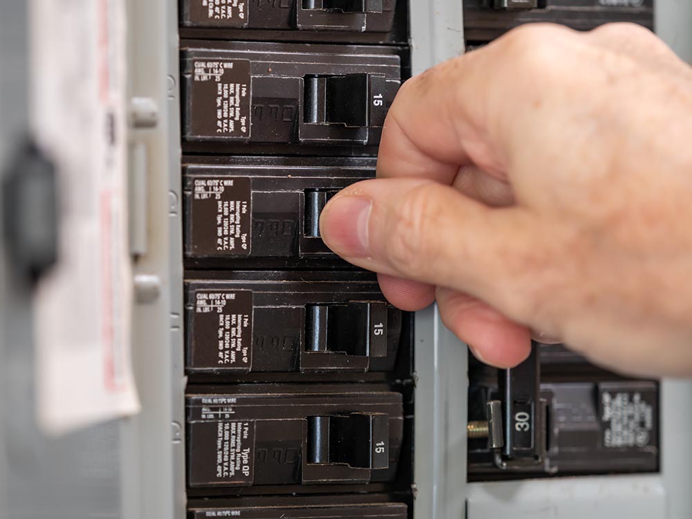 A hand adjusting a circuit breaker in a breaker panel.