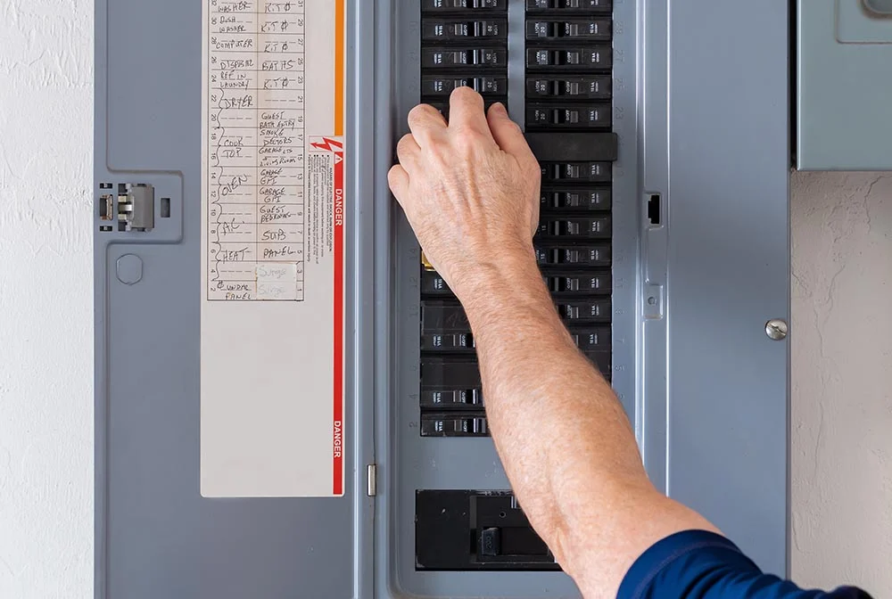 A person is adjusting the switches on a circuit breaker panel.