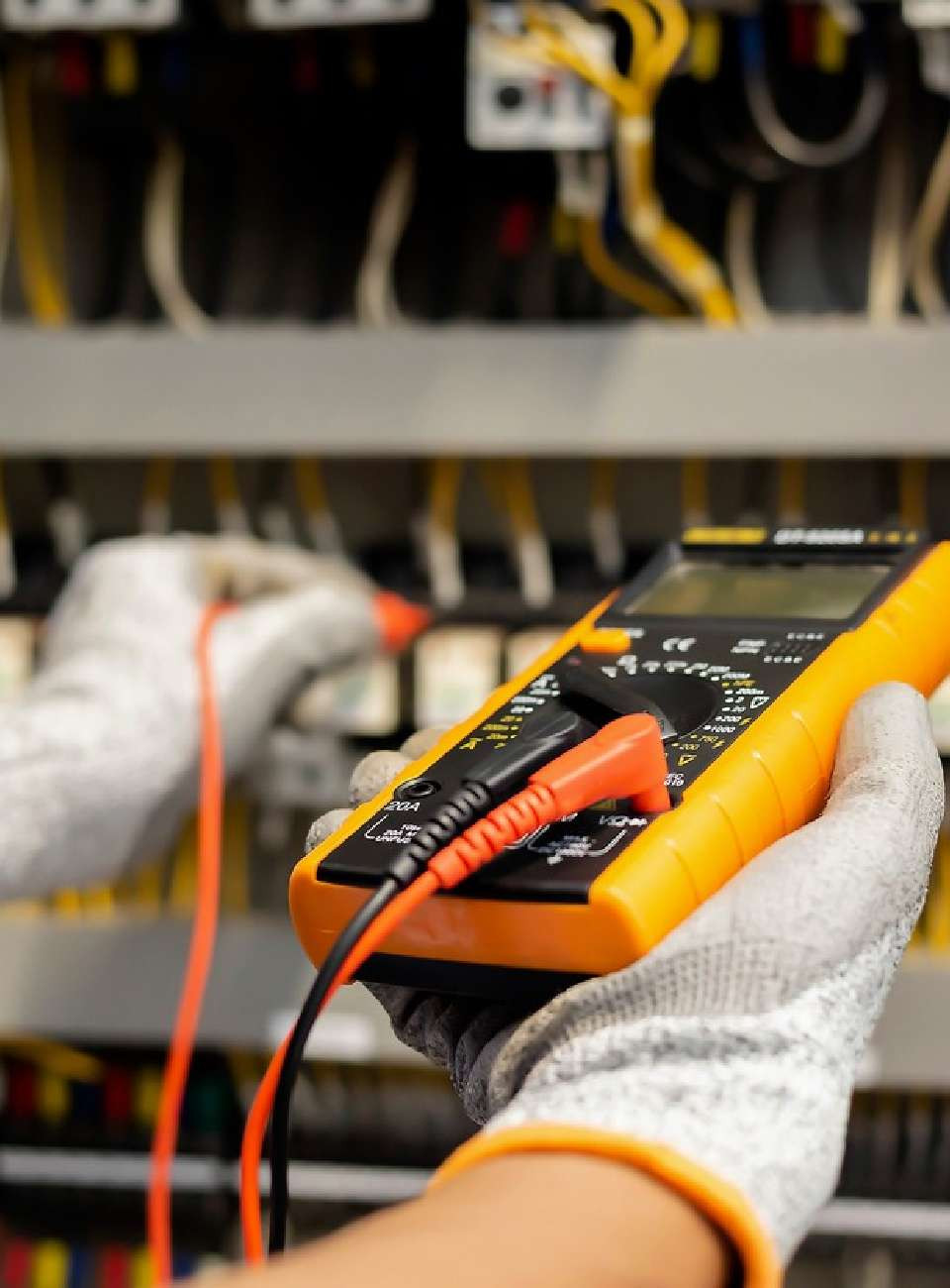 A person wearing a glove is using a digital multimeter to test electrical connections in a control panel.