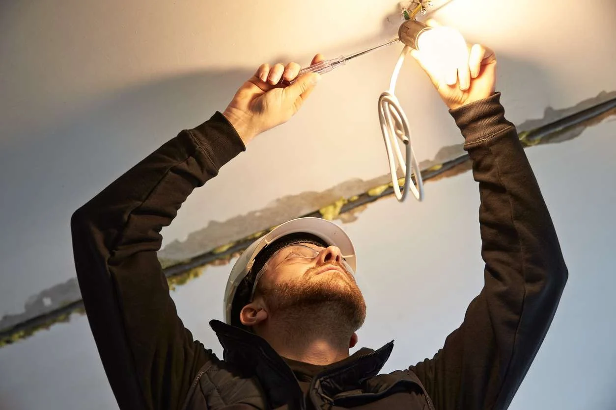 A man in a helmet is installing a light fixture on the ceiling.