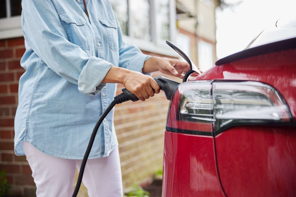 A person plugging in a charging cable to the rear of a red electric vehicle.