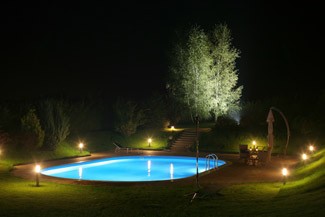 A serene backyard pool illuminated at night, surrounded by greenery and soft outdoor lighting.