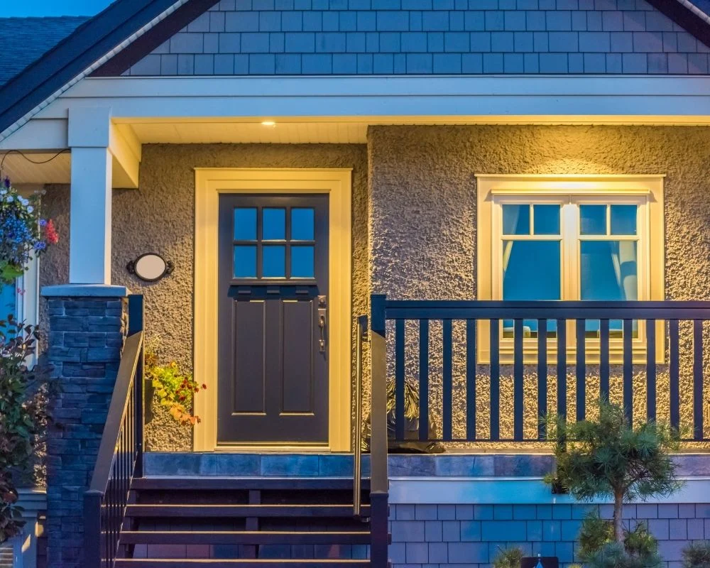 A well-lit entrance of a house featuring a blue door, a small porch with railing, and a window above the door.