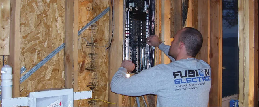 A man working on a circuit breaker box in a wooden frame wall.